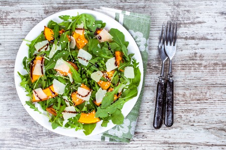 Salad with baked pumpkin, arugula, parmesan and sesame on wooden backgroundの写真素材