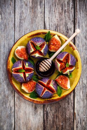 Fresh ripe figs with honey and mint leaves on a rustic wooden tableの写真素材