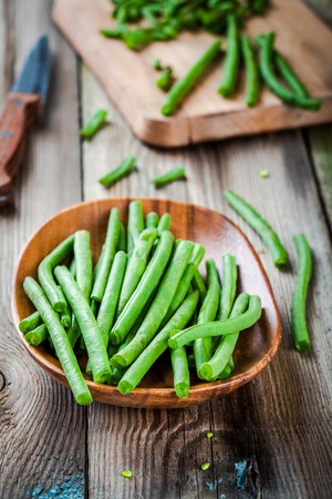 pods of fresh organic green beans in a wooden bowl on a rustic tableの写真素材