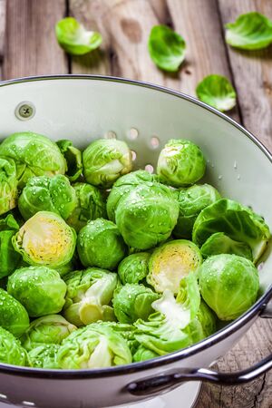Fresh organic Brussels sprouts in a colander on a wooden tableの写真素材