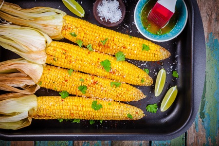 baked sweet corn cobs with herb butter and lime on wooden tableの写真素材