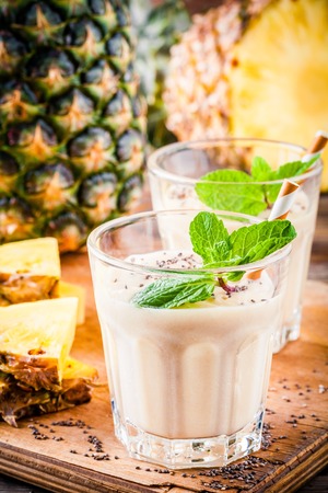 Pineapple smoothie with banana, chia seeds and mint on wooden backgroundの写真素材