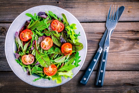 Fresh salad with mixed greens and cherry tomato in bowl on wooden backgroundの写真素材