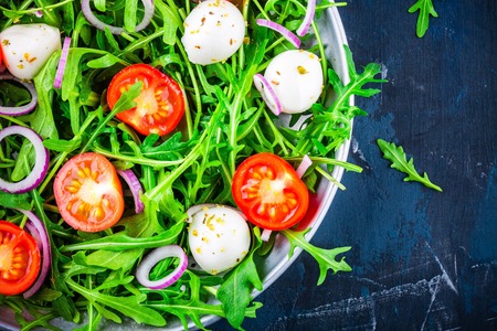 fresh green salad with arugula, tomatoes, mozzarella and red onion on dark backgroundの写真素材
