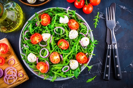 fresh green salad with arugula, tomatoes, mozzarella and red onion on dark backgroundの写真素材