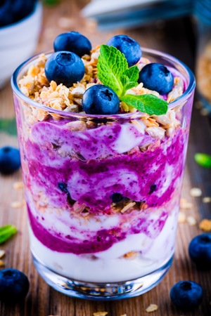 Yogurt parfait with granola, fresh blueberry and mint in a glass on wooden backgroundの写真素材