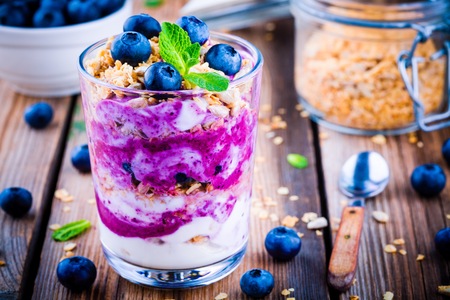 Yogurt parfait with granola, fresh blueberry and mint in a glass on wooden backgroundの写真素材