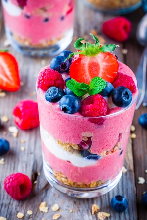 Healthy breakfast: yogurt parfait with granola and raspberry, blueberry and strawberry on wooden backgroundの写真素材