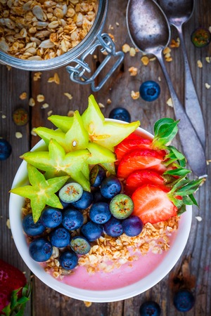 Healthy breakfast bowl: raspberry smoothies with granola, blueberries, strawberries and starfruit on wooden backgroundの写真素材