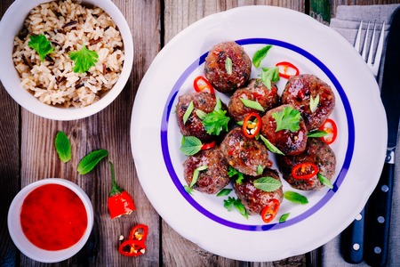 homemade meatballs with wild rice, mint, green onions and chili sauce on wooden tableの写真素材
