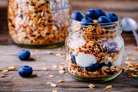 Healthy breakfast parfait with yogurt,  homemade granola and fresh bluberries in glass jar on wooden backgroundの写真素材