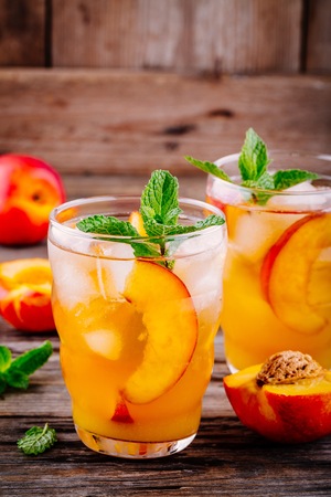 Summer cold drinks: homemade peach ice tea with ice cubes, and mint in glass on wooden backgroundの写真素材