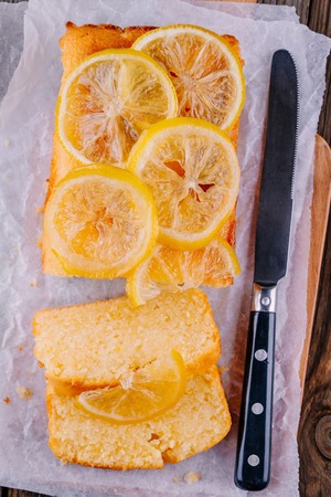 Lemon loaf cake with candied lemon slices on wooden background. Top view