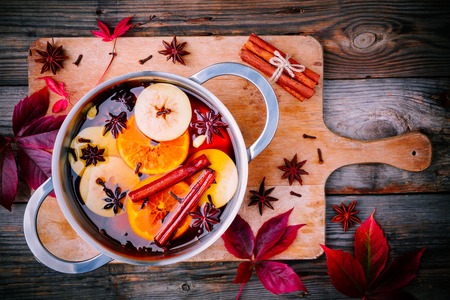 Hot mulled cider drink with citrus, apples, cinnamon sticks, cloves and anise in cooking pan on wooden backgroundの写真素材