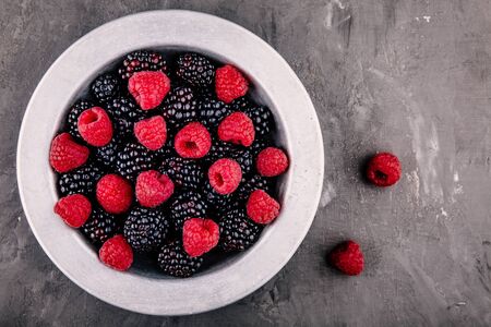 fresh ripe organic raspberries and blackberries in a bowl on a gray rustic background