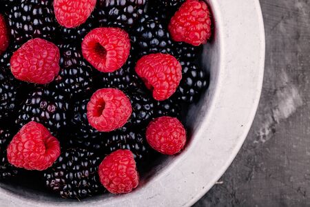 Fresh ripe organic raspberries and blackberries in a bowl on rustic backgroundの写真素材