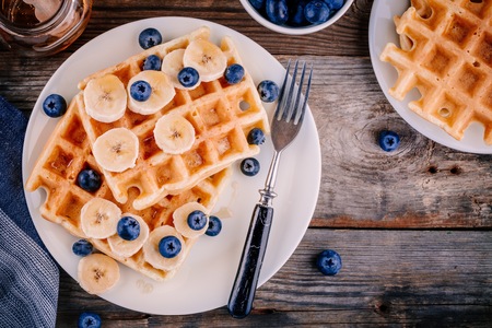 Fresh homemade belgian waffles with blueberries and banana for breakfast on wooden background.の写真素材