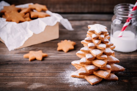 Homemade baked Christmas gingerbread tree with icing sugar on wooden background.