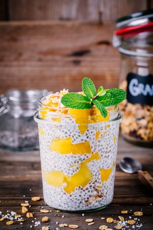 healthy vegan breakfast, chia pudding with mango and granola in the jar on wooden rustic backgroundの写真素材