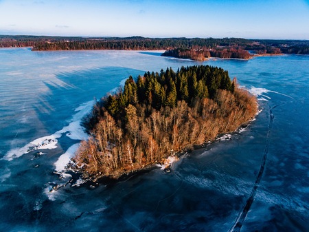 Aerial view of the winter snow covered forest and frozen lake from above captured with a drone in Finland.の写真素材