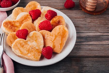 Heart shaped pancakes with raspberries and honey for St. Valentine's Day on wooden baclgroundの写真素材