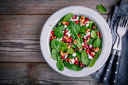 Fresh green salad with spinach, walnuts, feta cheese and pomegranate on wooden backgroundの写真素材