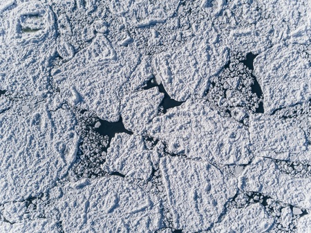 Aerial view over the surface of sea and cracked ice under the snow