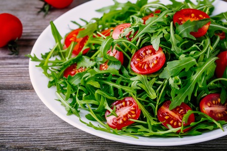 fresh green salad with arugula and red tomatoes on rustic wooden backgroundの写真素材