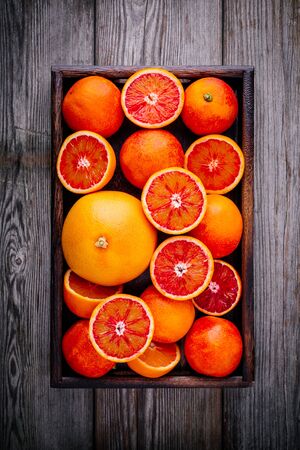 Sliced and whole ripe juicy Sicilian Blood oranges and grapefruit in the box on wooden background. Top viewの写真素材
