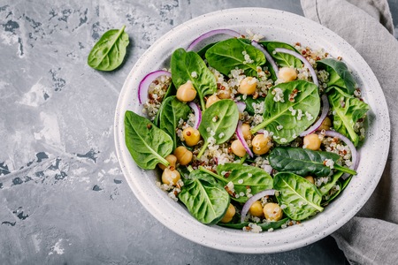 Healthy green salad bowl with spinach, quinoa, chickpeas and red onions on gray backgroundの写真素材