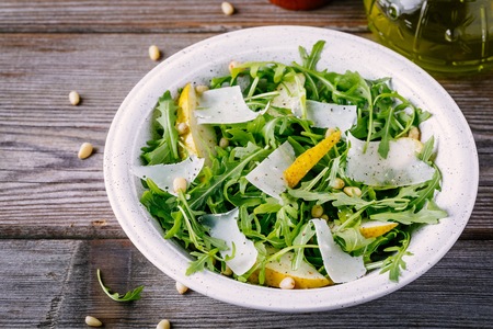 green salad bowl of arugula with pear, parmesan cheese and pine nuts on a wooden background