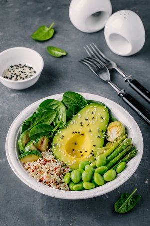 Healthy green vegetarian buddha bowl salad with grilled vegetables and quinoa, spinach, avocado, brussels sprouts, zucchini, asparagus, edamame beans with sesame seeds on dark gray background. Top view.の写真素材