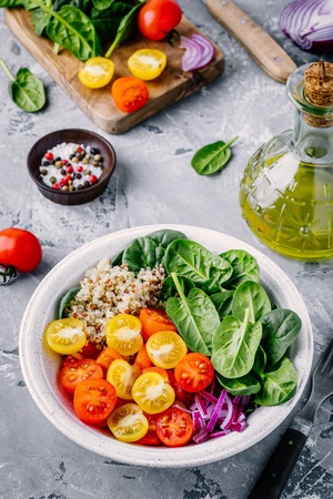 Healthy green bowl salad with spinach, quinoa, yellow and red tomatoes, onions and seeds on gray backgroundの写真素材