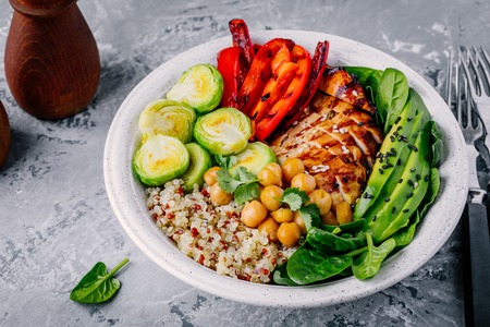Healthy vegetable buddha bowl lunch with grilled chicken and quinoa, spinach, avocado, brussels sprouts, red paprika and chickpea on gray background. の写真素材