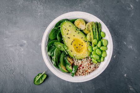 Healthy green vegetarian buddha bowl salad with grilled vegetables and quinoa, spinach, avocado, brussels sprouts, zucchini, asparagus, edamame beans with sesame seeds on dark gray background. Top view.の写真素材