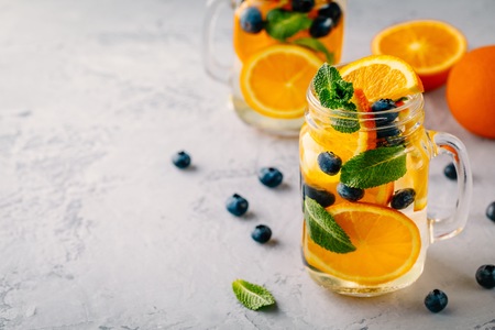 Infused detox water with orange, blueberry and mint. Ice cold summer cocktail or lemonade in glass...