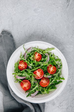 Green salad arugula with tomatoes and red onion in bowl. Top viewの写真素材