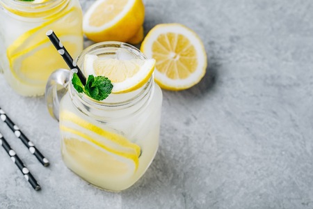 Homemade refreshing summer lemonade drink with lemon slices and ice in mason jars with straw and mintの写真素材