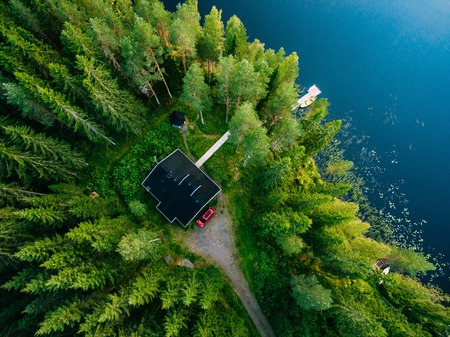 Aerial view of wooden cottage in green pine forest by the blue lake in rural summer Finlandの写真素材