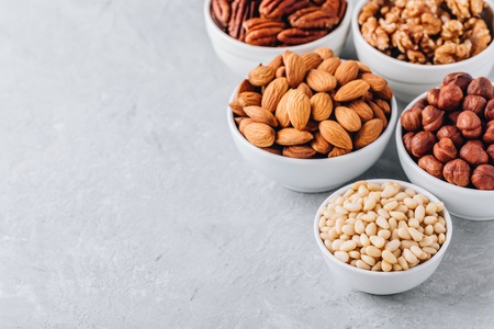 Pine nuts, almonds, pecans, walnuts and hazelnuts in white bowls on grey background. Mixed nuts. Healthy food and snack. Copy spaceの写真素材