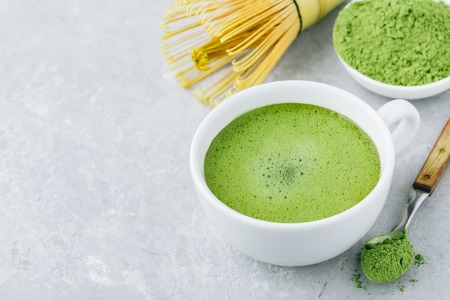 Japanese matcha green tea latte in white cup on gray stone background.