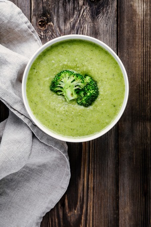 Homemade broccoli cream soup in white bowl with toasts on wooden rustic background. Top viewの写真素材