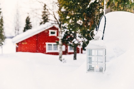 Christmas candle in lantern. Red wooden cottage in rural snowy Finland. Winter landscape.の写真素材