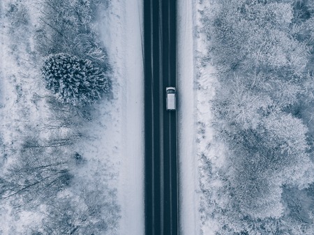Aerial view of country road going through the beautiful snow covered landscape. Drone photography.