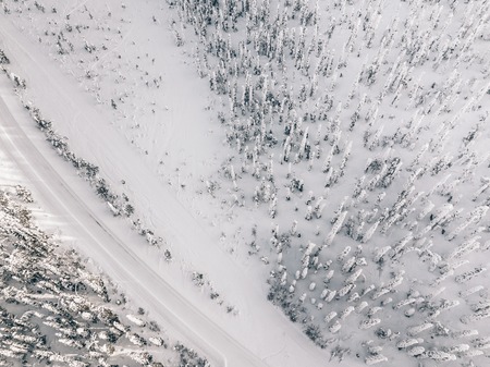 Aerial view of snow covered winter forest and road. Beautiful rural landscape in Finland, Lapland.