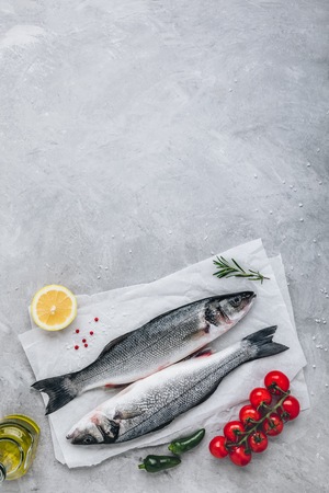 Fresh raw fish sea bass (seabass) with rosemary and vegetables on gray stone background. Top view.の写真素材
