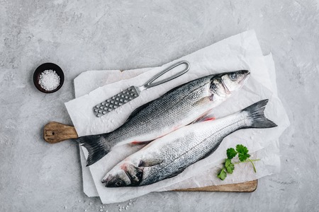 Fresh raw fish sea bass (seabass) with parsley and sea salt on gray stone background. Top view.の写真素材