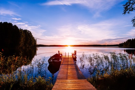 Wooden pier with fishing boat at sunset on a lake in rural Finlandの写真素材