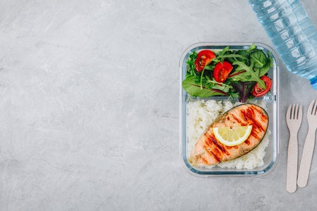 Meal prep containers with salmon and rice, green mix salad with tomatoes. Top view, copy spaceの写真素材