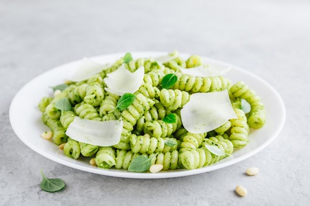 Fusilli pesto pasta with pine nuts, basil leaves and parmesan slicesの写真素材